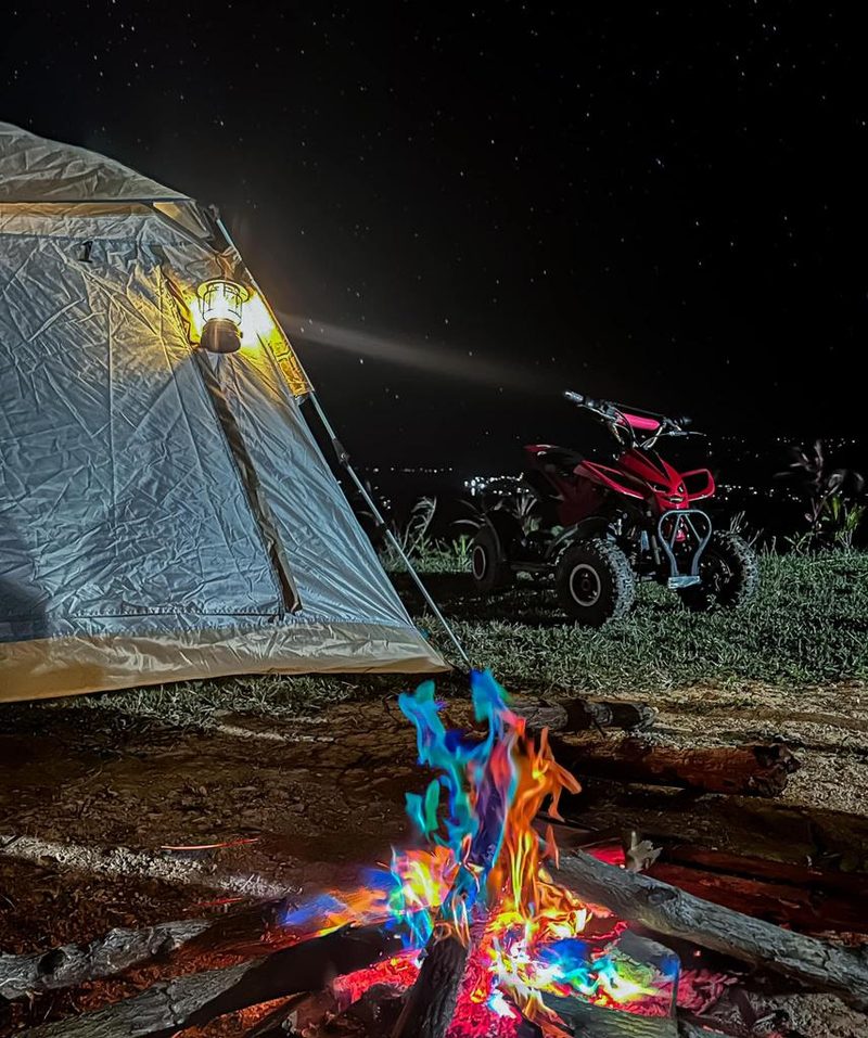 A tent pitched on the ridge beside a bonfire under a sky full of stars
