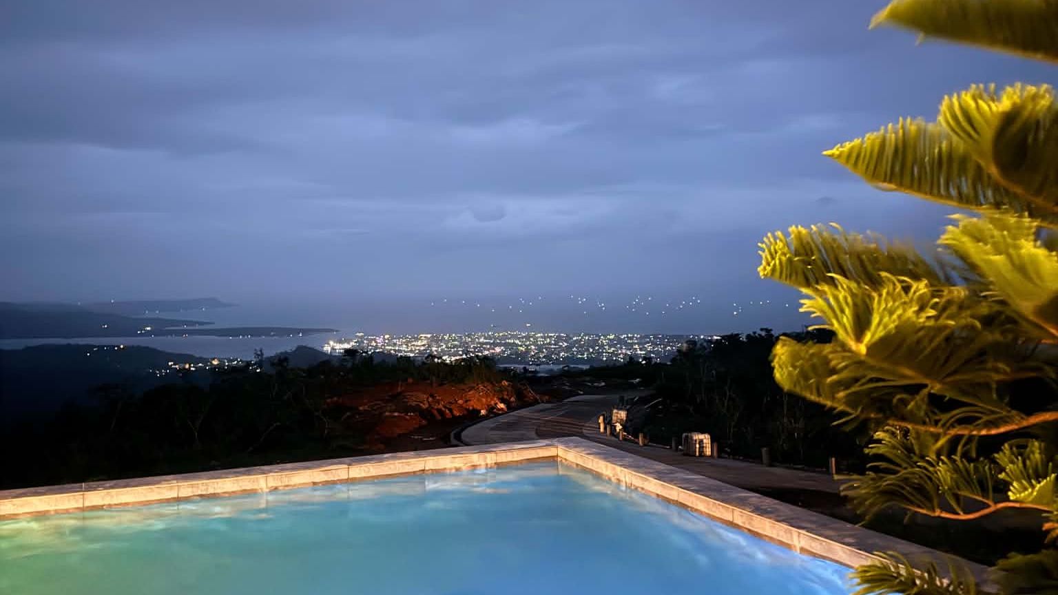 The infinity pool at Valle Justina at blue hour, with the lights of Masbate City across the bay
