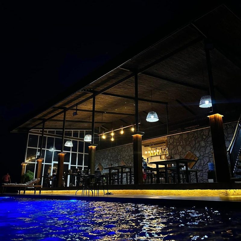 The pavilion and pool lit at night, seen from the water's edge